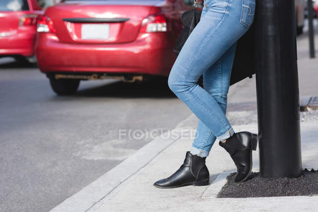 Низька частина жінки, що спирається на вуличний полюс у місті — стокове фото