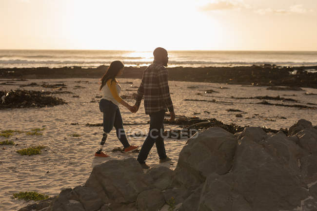Coppia che si tiene per mano e cammina sulla spiaggia durante il tramonto — Foto stock
