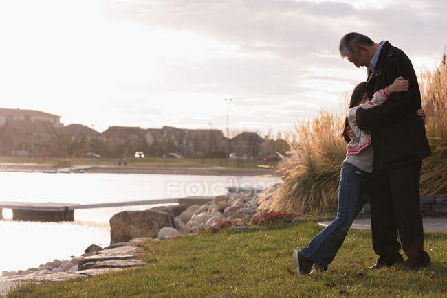 Grand-père et petite-fille se serrant dans leurs bras près du lac — Photo de stock