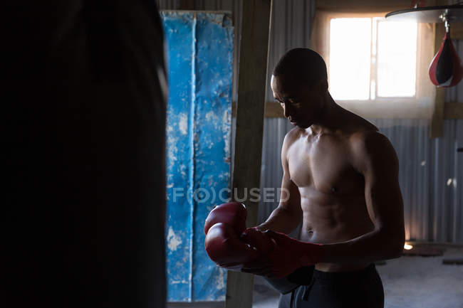 Shirtless boxeador masculino de pé com luvas de boxe no clube de boxe — Fotografia de Stock