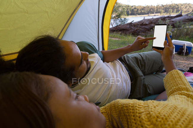 Casal jovem usando telefone celular na barraca no parque de campismo — Fotografia de Stock