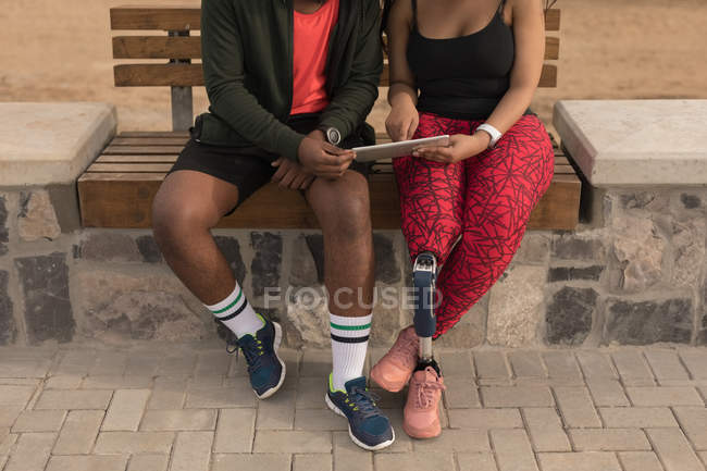 Section basse du couple discutant sur tablette numérique sur banc de promenade — Photo de stock
