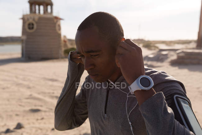 Atleta masculino usando fone de ouvido perto da praia em um dia ensolarado — Fotografia de Stock