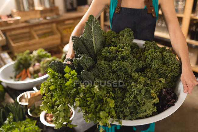 Mid section of female staff holding basket of vegetables in supermarket — Stock Photo