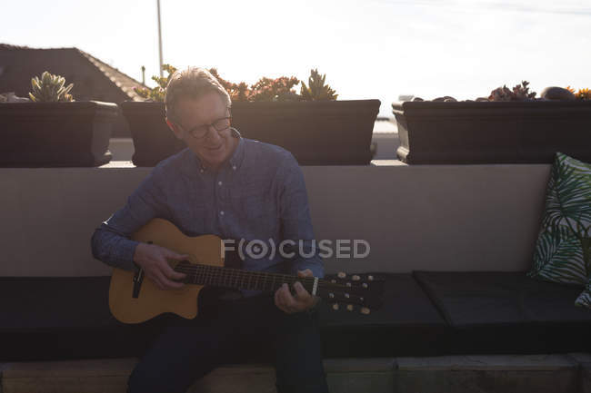 Homme âgé jouant de la guitare en terrasse le jour ensoleillé — Photo de stock