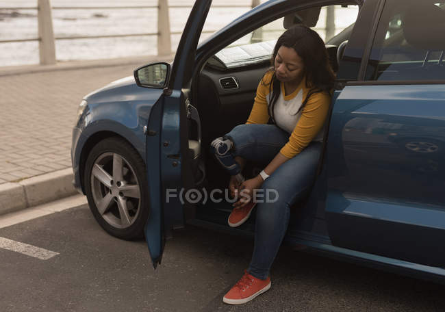 Beautiful disabled woman tying shoelace while sitting in car — Stock Photo