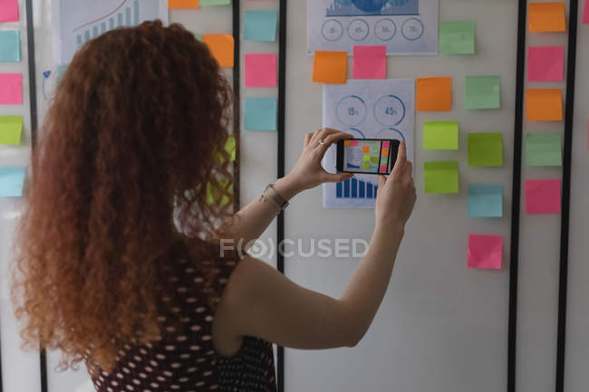 Female executive taking photo of sticky notes in office — Stock Photo