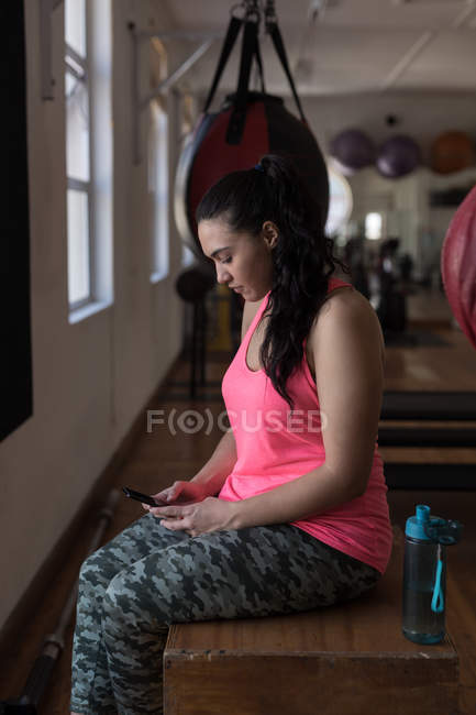 Vista lateral del boxeador femenino utilizando el teléfono móvil en el gimnasio - foto de stock