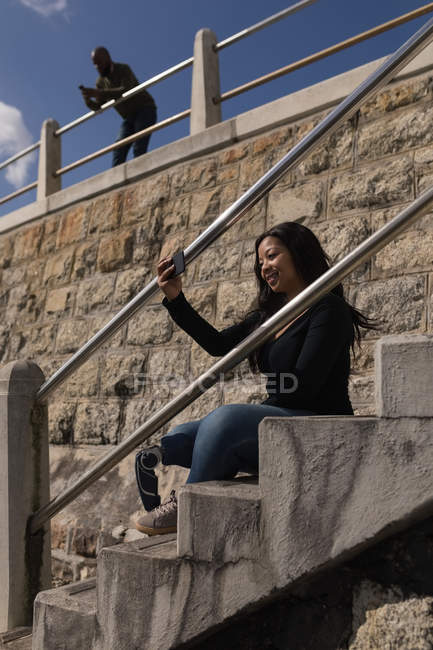 Donna sorridente che fa selfie sulle scale del lungomare — Foto stock