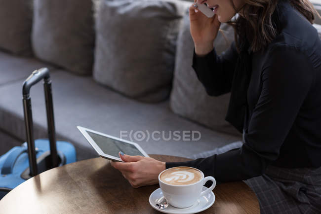 Середній розділ ділової жінки, що розмовляє на мобільному телефоні, використовуючи цифровий планшет в готелі — стокове фото