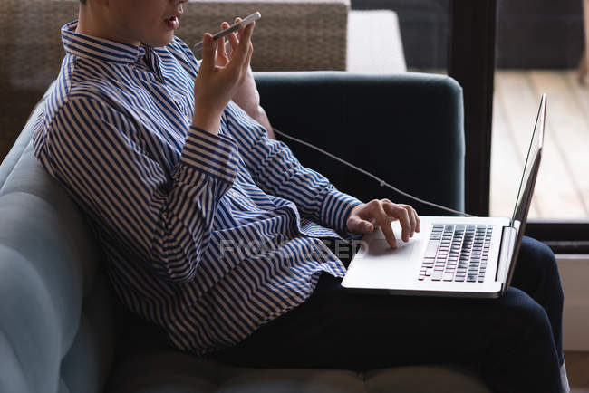 Чоловік виконавчої розмови на мобільному телефоні при використанні ноутбука в офісі — стокове фото