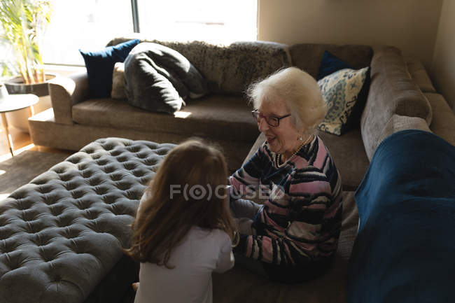 Abuela y nieta interactuando entre sí en el sofá en la sala de estar en casa - foto de stock