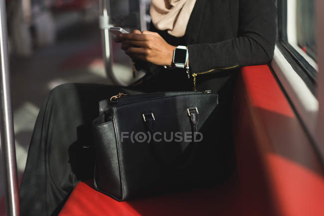 Средняя секция женщины, пользующейся мобильным телефоном во время поездки на поезде — стоковое фото
