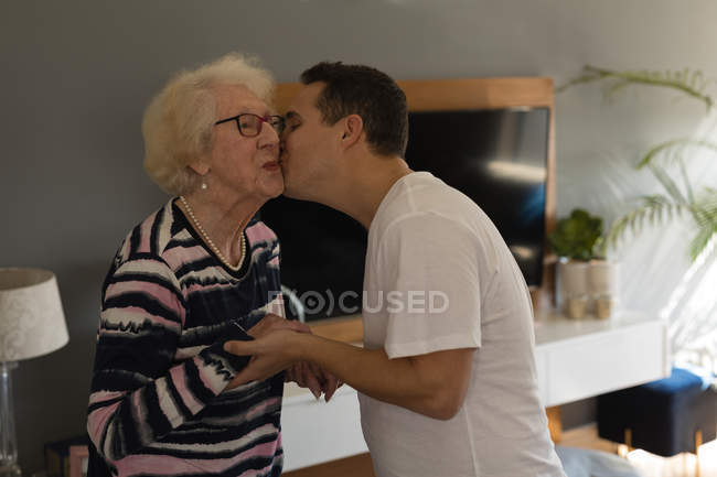 Sohn küsst seine Mutter zu Hause im Wohnzimmer — Stockfoto