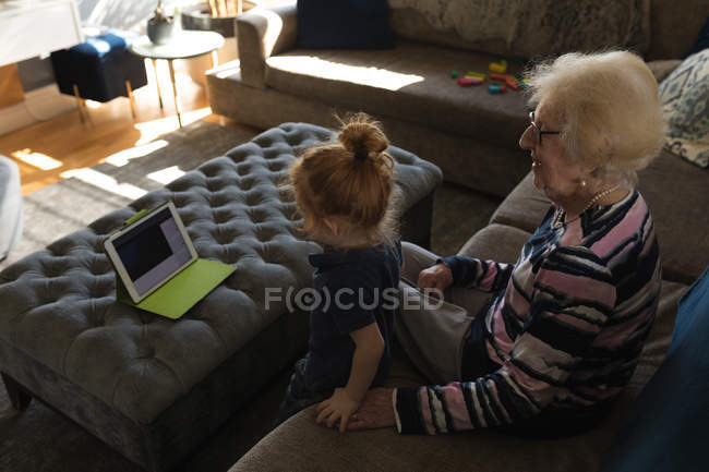 Grandmother and granddaughter making video call on digital tablet in living room at home — Stock Photo