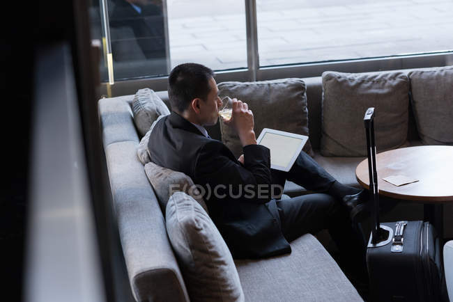 Geschäftsmann trinkt Whiskey mit digitalem Tablet im Hotel — Stockfoto