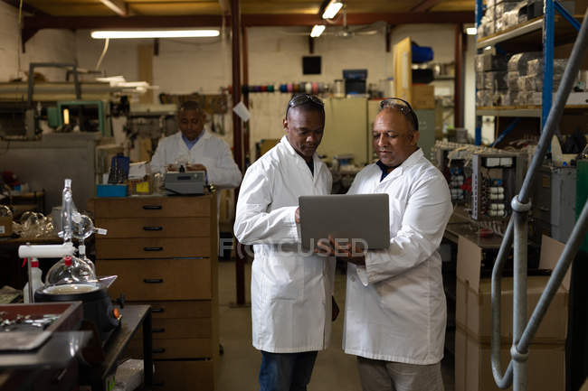 Deux travailleurs masculins discutent sur un ordinateur portable dans une usine de verre — Photo de stock