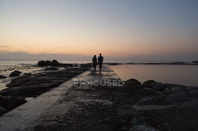 Vue arrière du couple marchant sur la promenade près du bord de mer — Photo de stock