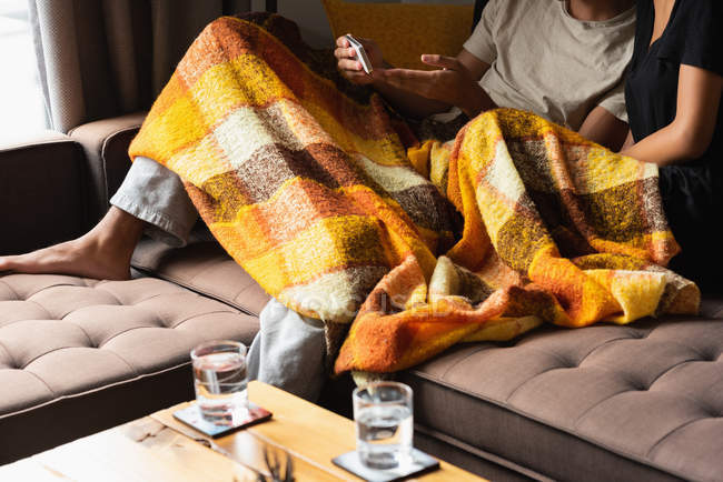 Low section of couple using mobile phone on sofa in living room at home — Stock Photo