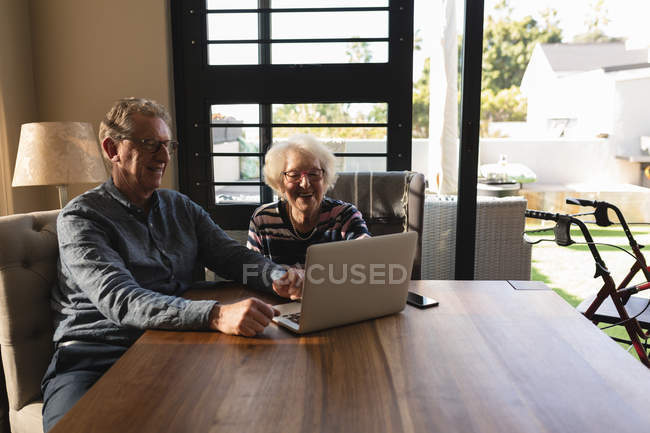 Pareja mayor usando portátil en la mesa en la sala de estar en casa - foto de stock