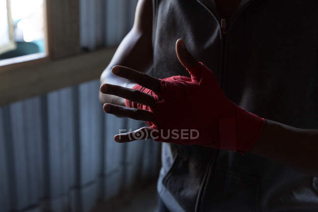 Primer plano del boxeador masculino atando envoltura de mano en la mano en el club de boxeo - foto de stock