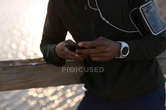 Mid section of male athlete using mobile phone on pier — Stock Photo