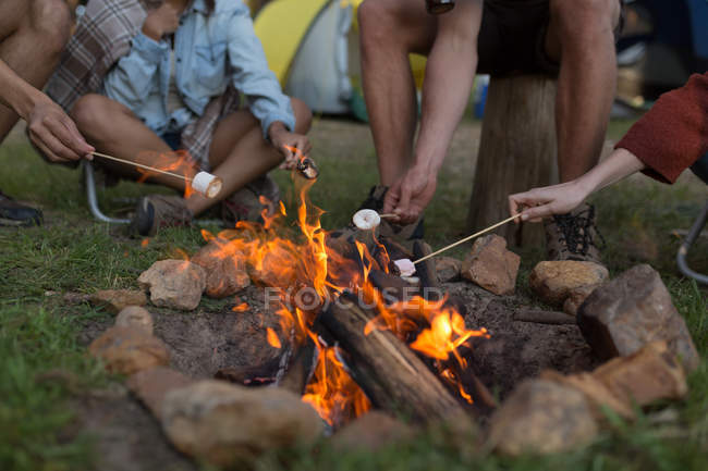 Gros plan d'un groupe d'amis rôtissant la guimauve sur un feu de camp — Photo de stock