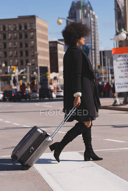 Femme avec sac à bagages marchant en ville par une journée ensoleillée — Photo de stock