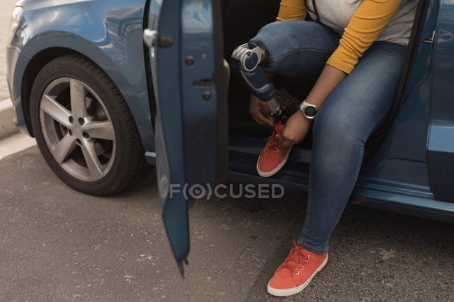 Низкая часть женщины-инвалида, завязывающей шнурки, сидя в машине — стоковое фото