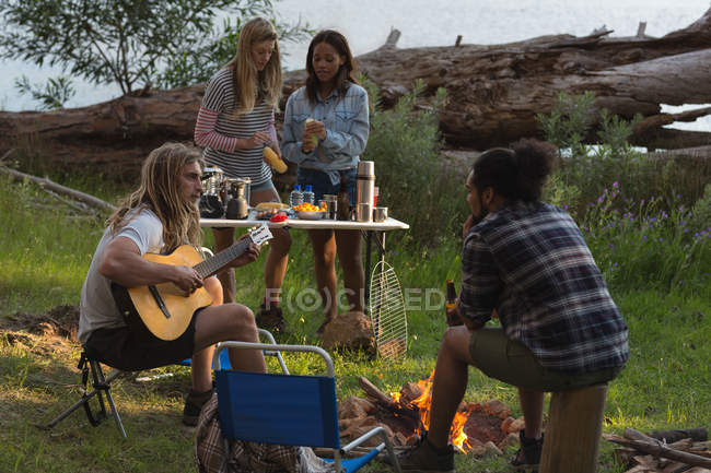 Grupo de amigos divirtiéndose cerca de la hoguera en el camping - foto de stock