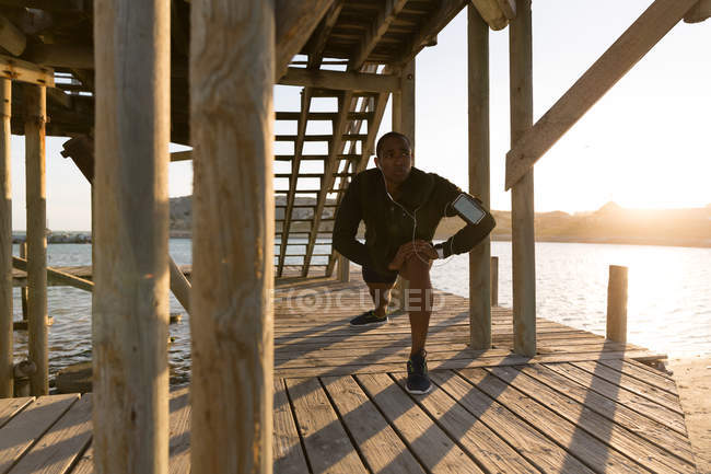 Hombre atleta estirándose en muelle en la playa - foto de stock