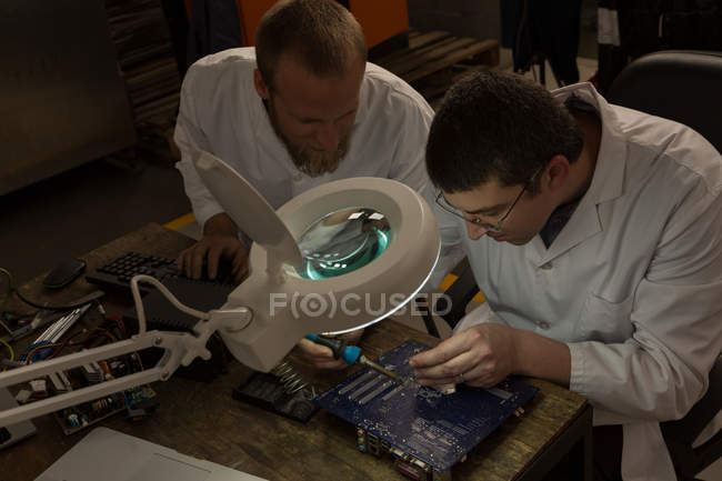 Robotics engineers assembling circuit board at desk in warehouse — Stock Photo