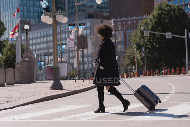 Mujer con bolsa de equipaje caminando en la ciudad en un día soleado - foto de stock