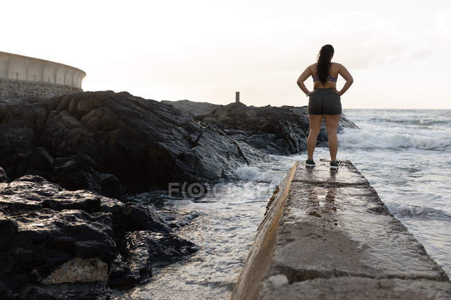 Rear view of female jogger standing at promenade near sea side — Stock Photo