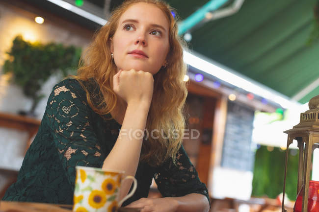 Задумчивая рыжая женщина отдыхает в кафе — стоковое фото