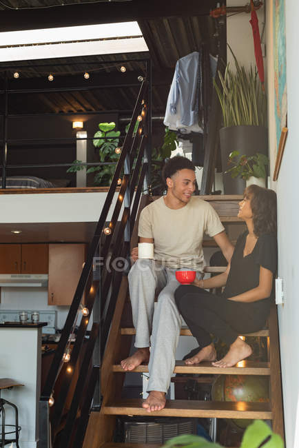 Couple interagissant les uns avec les autres tout en prenant un café dans les escaliers à la maison — Photo de stock