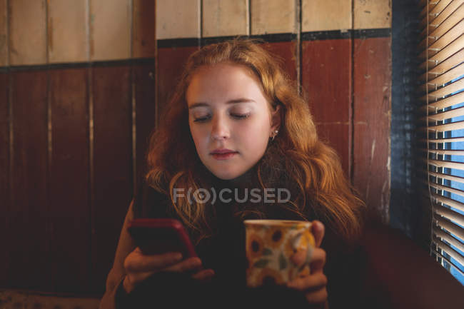 Руда жінці за допомогою мобільного телефону під час за кавою в кафе — стокове фото