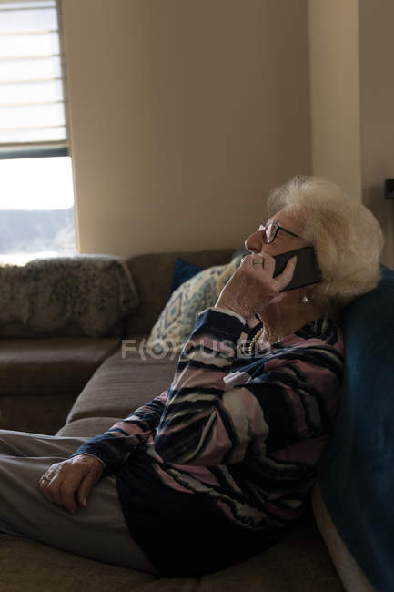 Mulher sênior conversando no telefone celular na sala de estar em casa — Fotografia de Stock