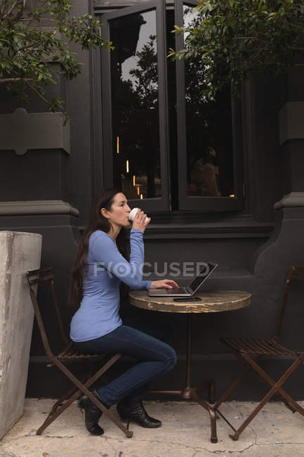 Hermosa mujer usando el teléfono móvil mientras toma café en la cafetería al aire libre - foto de stock