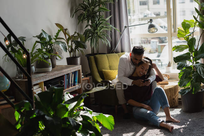 Casal usando telefone celular na sala de estar em casa — Fotografia de Stock