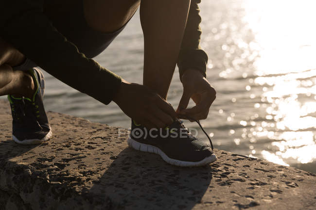 Atleta maschio legando i lacci delle scarpe sul muro di cinta in spiaggia — Foto stock