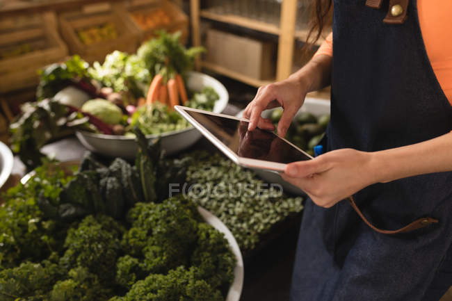 Sección media del personal femenino que utiliza tabletas digitales en el supermercado - foto de stock