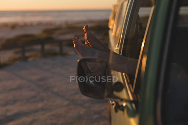 Woman's legs out of the car window on road trip — Stock Photo