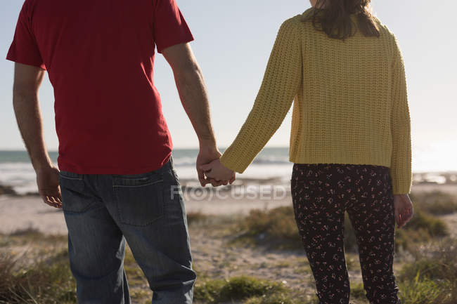 Sección media de la pareja tomados de la mano y de pie en la playa - foto de stock