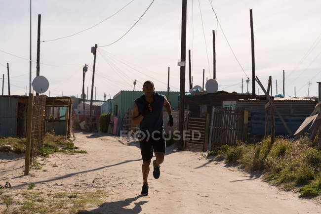 Чоловік-спортсмен біжить біля села в сонячний день — стокове фото