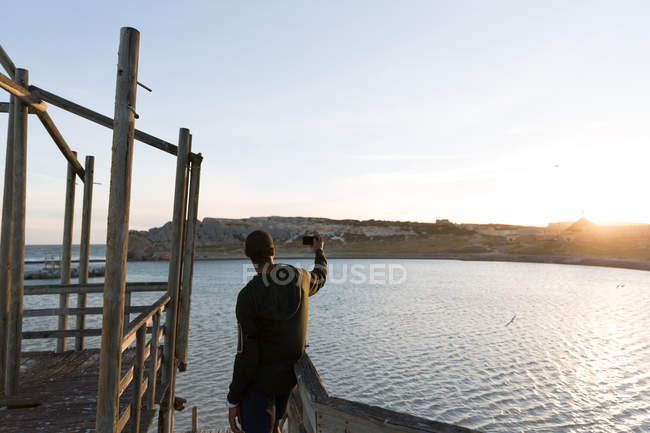 Rear view of male athlete taking selfie on pier — Stock Photo