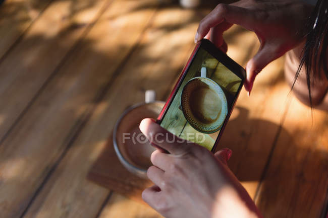 Primer plano de la mujer tomando fotos de la taza de café en la cafetería - foto de stock