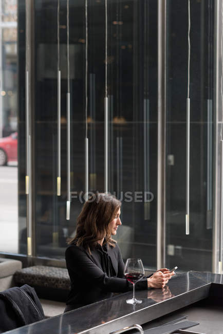 Geschäftsfrau trinkt Rotwein, während sie Handy im Hotel benutzt — Stockfoto