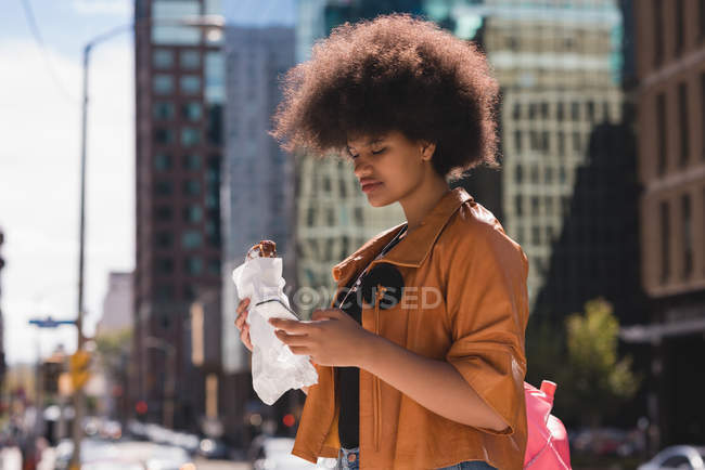 Женщина, пользующаяся мобильным телефоном во время еды в городе — стоковое фото
