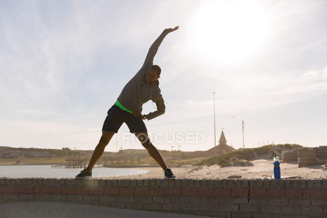 Atleta masculino haciendo ejercicio en la pared circundante cerca de la playa - foto de stock